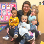teacher holding three kids in classroom